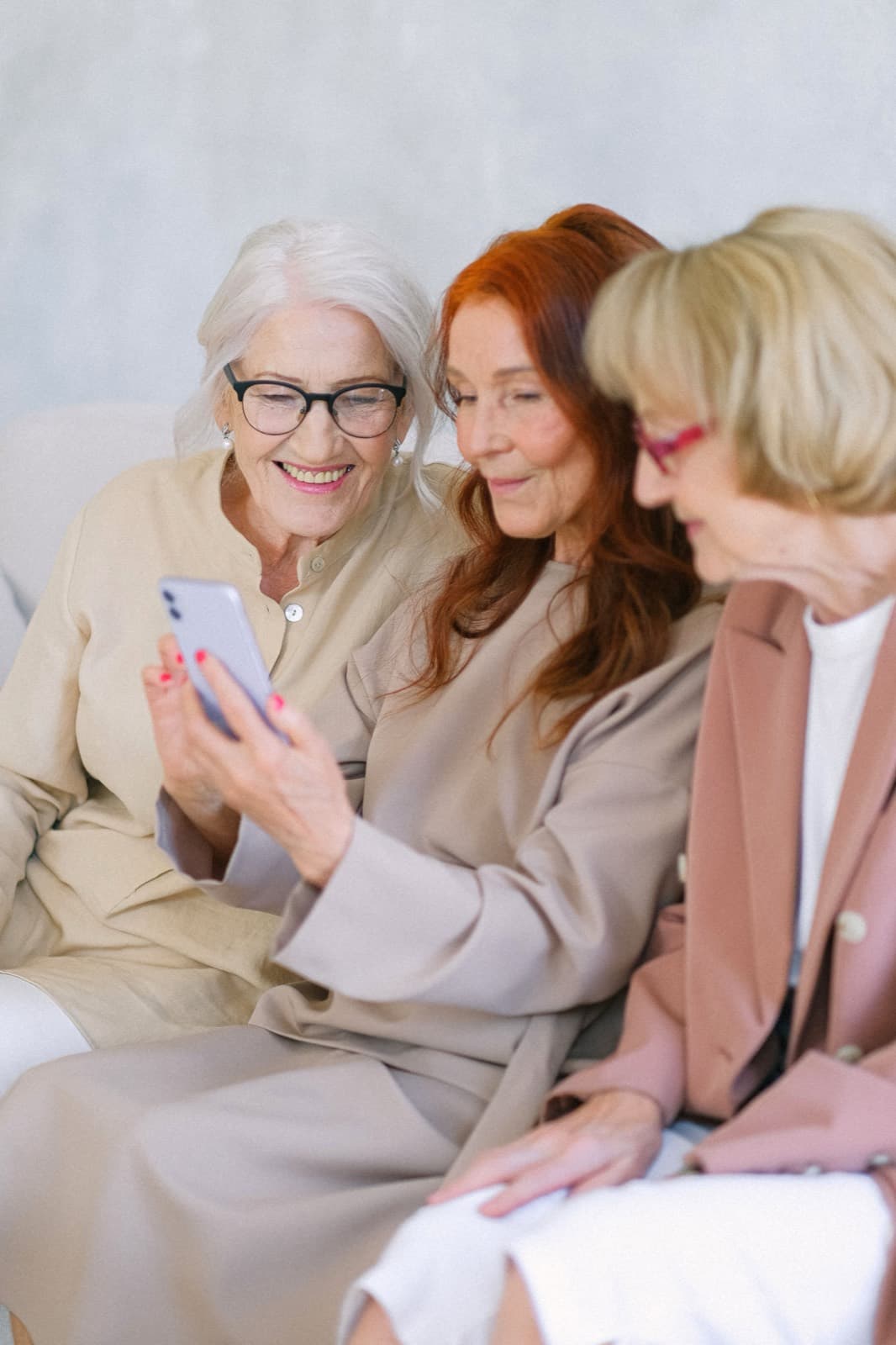 Three friends sitting together, laughing at something on a phone one of them is holding.