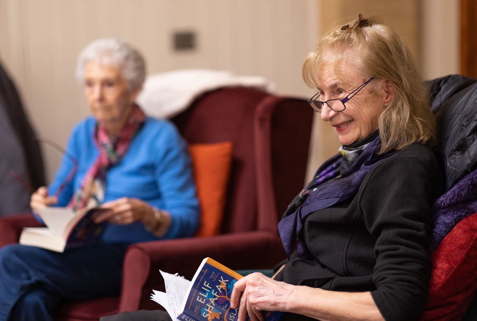 Two women sitting in armchairs, reading and talking together.